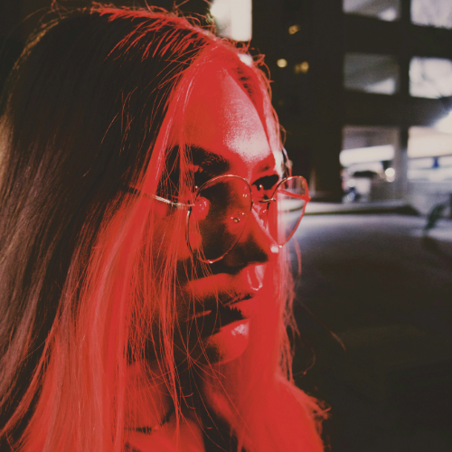 Close-up of a young woman in red lighting with glasses in a city at night, symbolizing modern consumer identity, culture, and the evolving automotive journey.